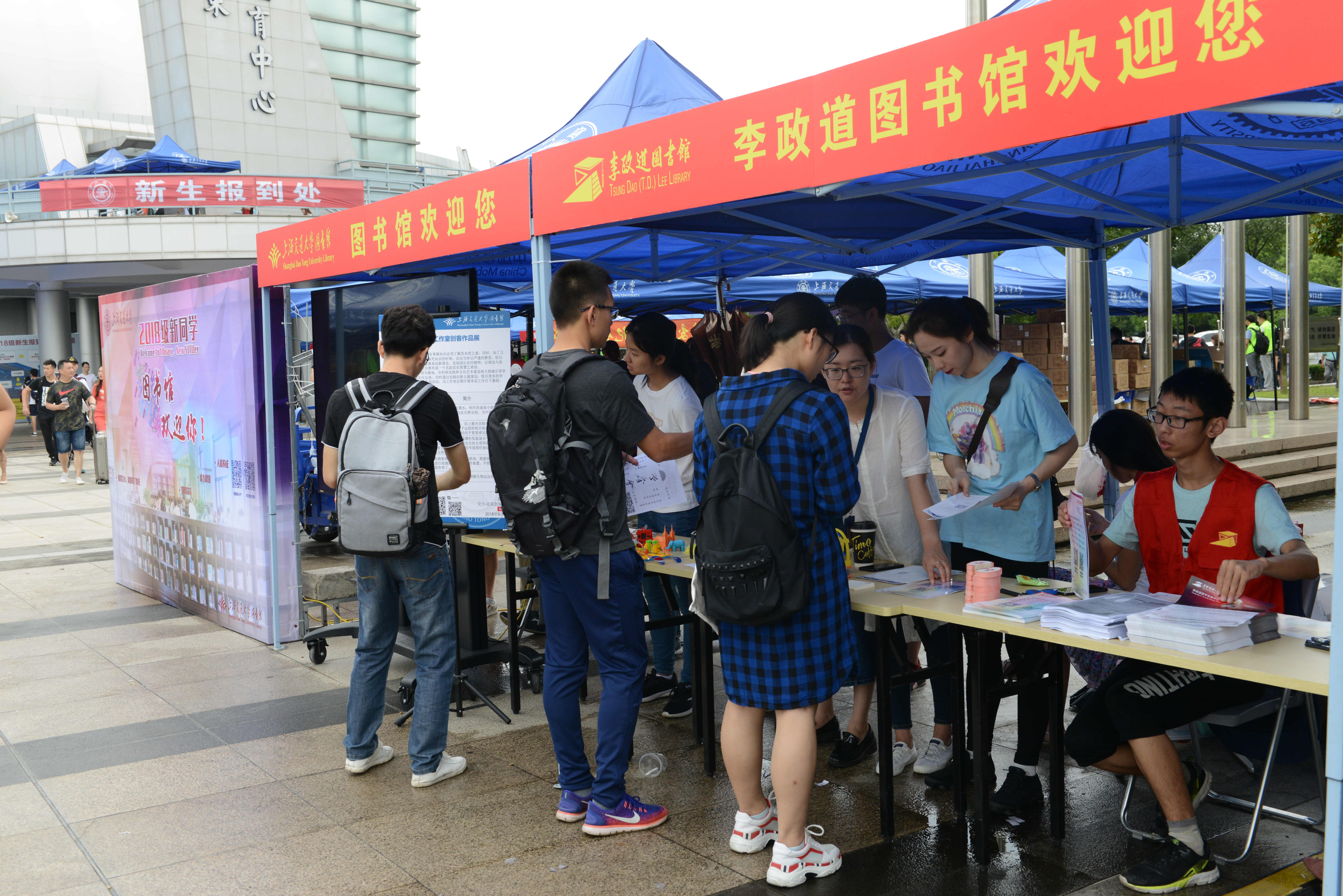 斜风细雨,秋意渐浓。9月8日清晨,交大图书馆2018级迎新日活动有条不紊地拉开帷幕。此次活动线上、线下同步推进,在图书馆官方微博直播迎新动态,在校园内分别设立了霍英东体育馆、图书馆主馆、包玉刚图书馆和李政道图书馆四个迎新点。图书馆馆员和学生志愿者们热情洋溢地在各自的岗位上迎接远道而来的新生。 还不到8点,新体育馆外“技术范儿”十足的迎新展台就吸引了不少学生和家长。图书馆创客空间的水上飞机、智能炸弹、3D打印模型,知了创新工作室参与研发的赛车等各式各样的学生作品让驻足围观的新生
